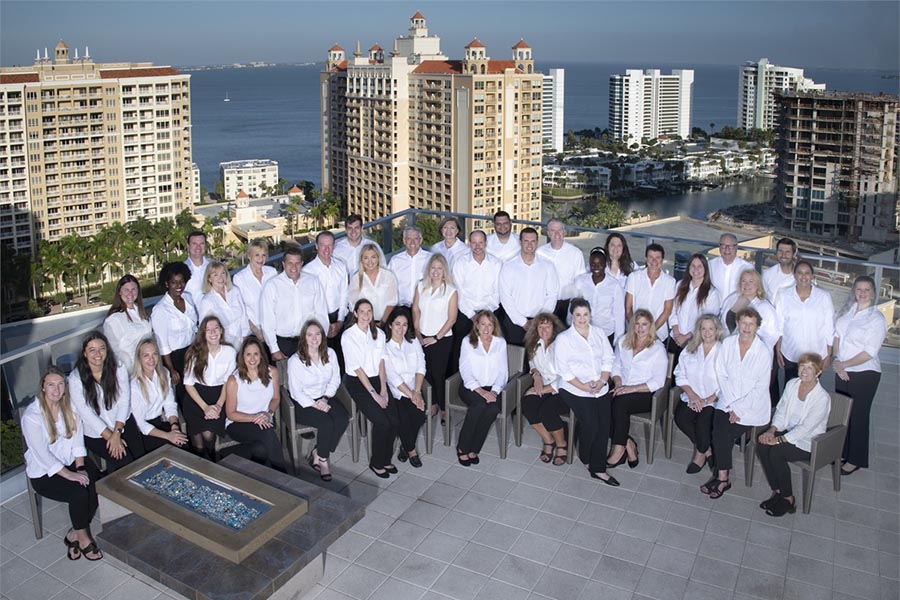 About Our Agency - Group Photo of Atlas Insurance Team Members Taken on a Stone Balcony Overlooking Sarasota Florida Buildings and Water